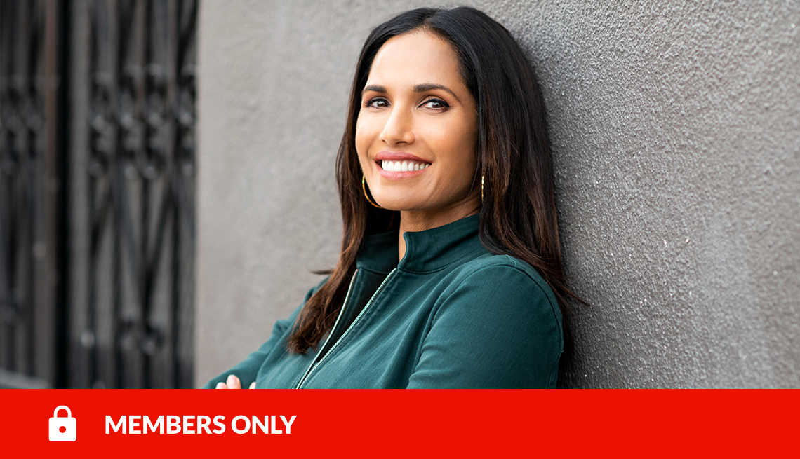padma lakshmi smiling with arms crossed and leaning against a gray wall, with red members only banner and lock icon