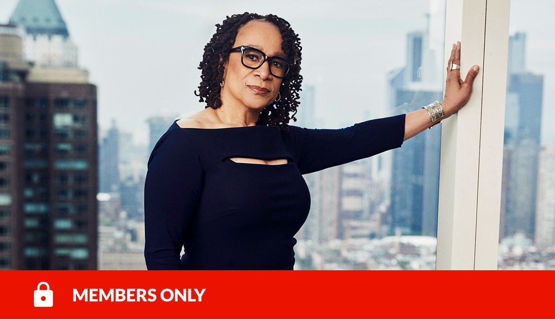 S. Epatha Merkerson in a black dress leaning against a window overlooking city buildings