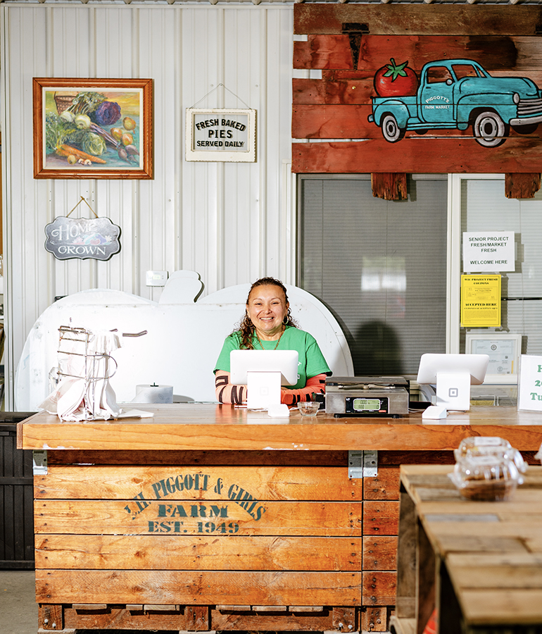 lucy mendoza at the counter of piggott's farm and bakery; signs and artwork behind her