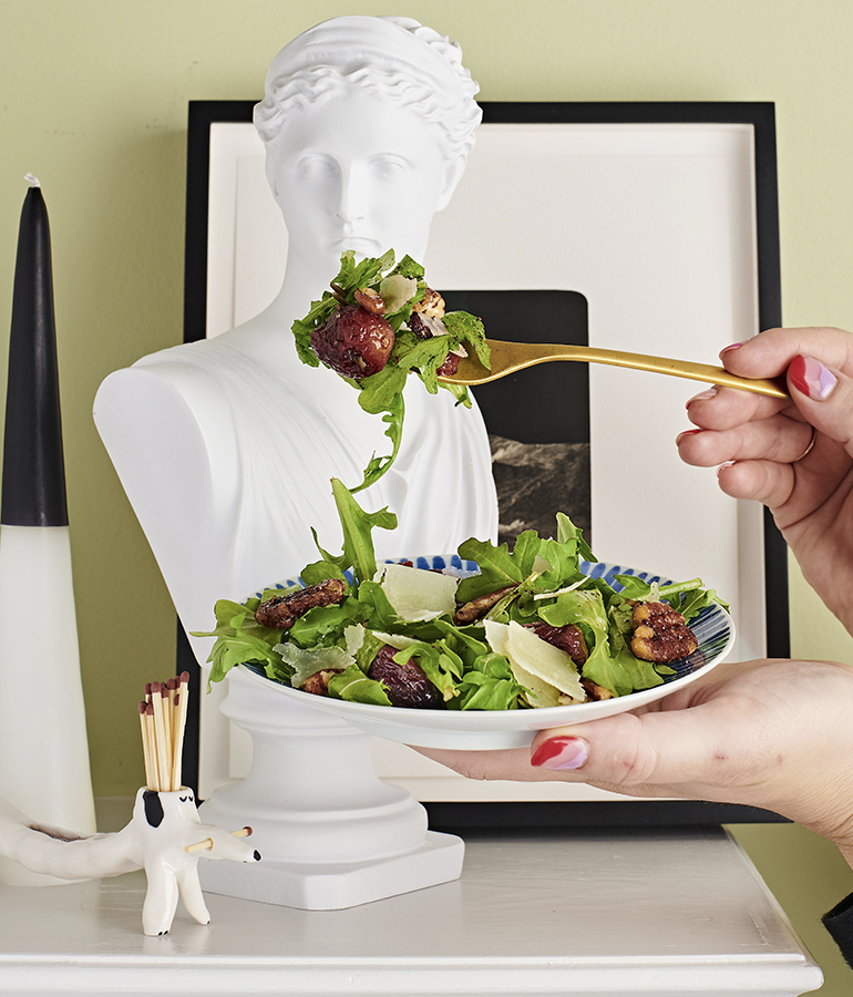 hand holding plate with salad on it; other hand holding fork with some of salad on it; in front of upper half body mannequin 
