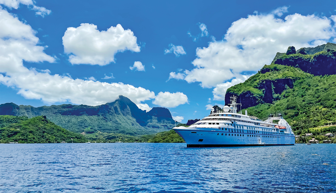 Cruise ship in body of water with trees and mountains in background