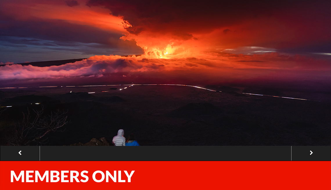 people watching the fiery moana loa volcano erupting into a pink and orange sky in the distance , with slideshow overlay and red members only banner