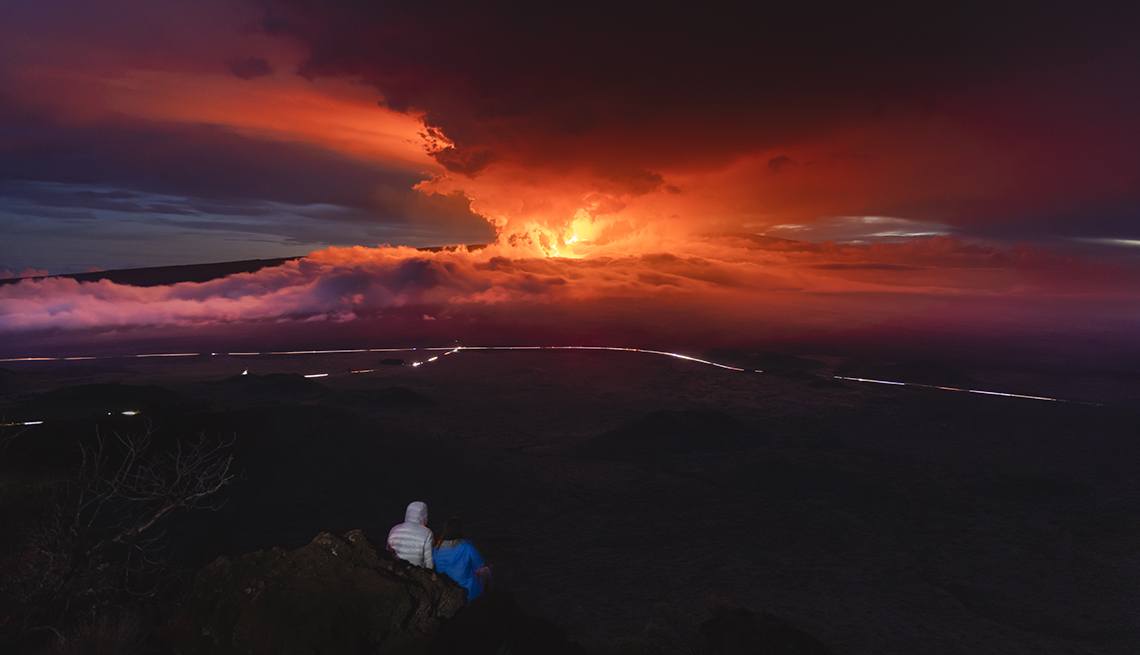 people watching the fiery moana loa volcano erupting into a pink and orange sky in the distance 