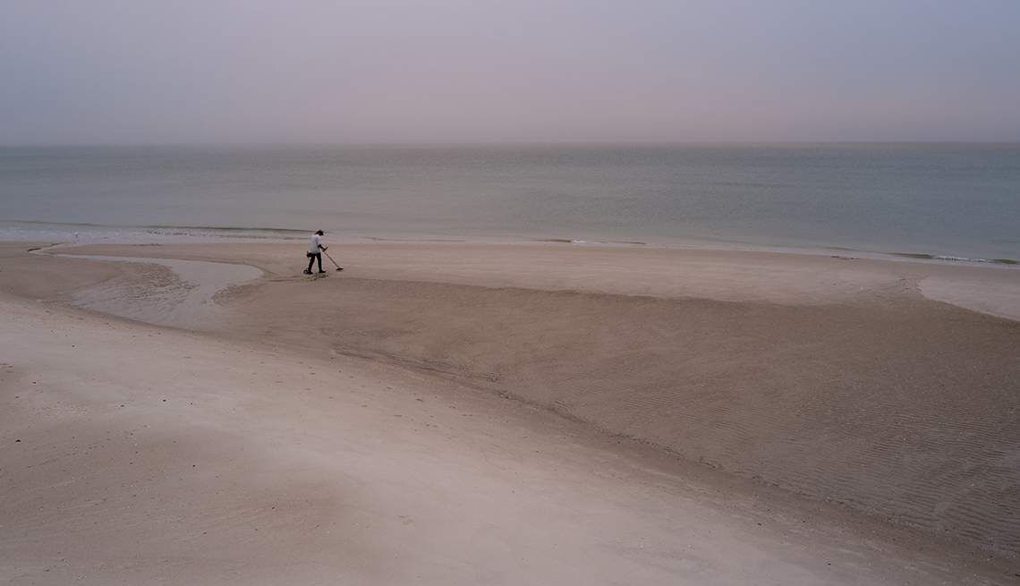 item 13 of Gallery image - a beachcomber with a metal detector alone on a beach on a gray day