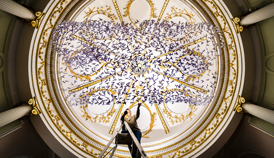 item 5 of Gallery image - a person stands on a ladder under hundreds of purple origami birds under an ornate gold and white roof and four columns