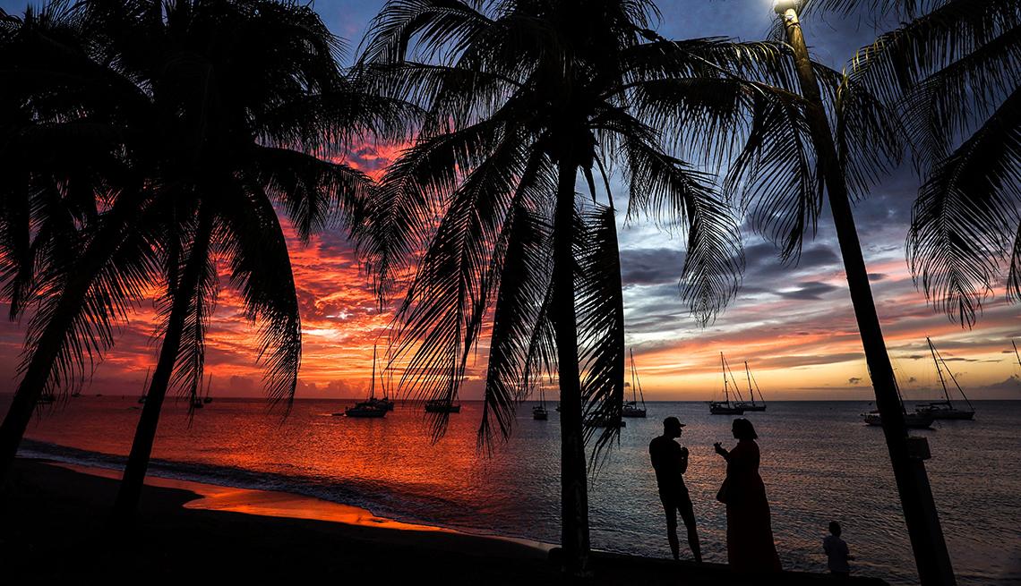 item 4 of Gallery image - pink and orange sunset over the water and silhouettes of sailboats, palm trees, and two adults and a child on the beach
