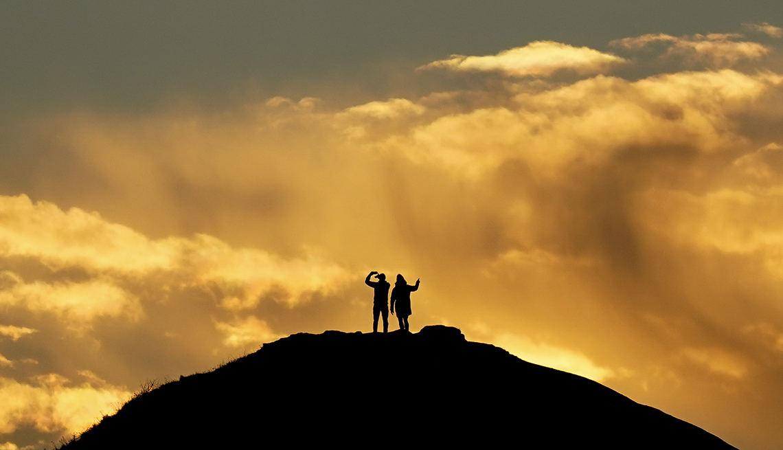 two people on a hill silhouetted against clouds lit up by the sunrise