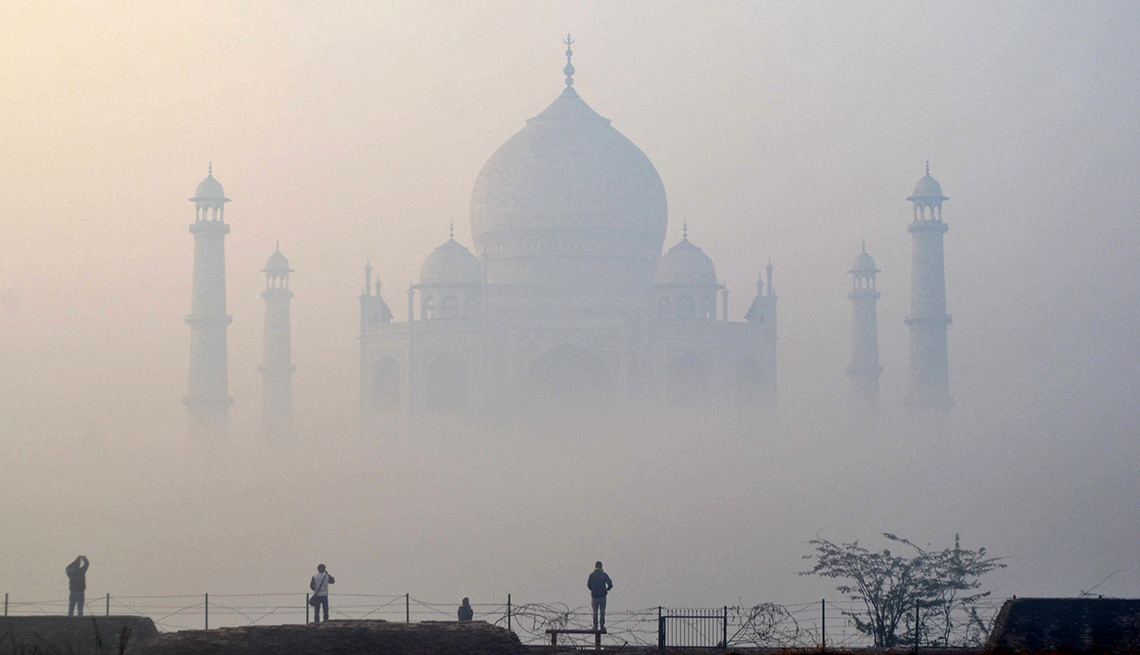 the taj mahal is shrouded in fog and four people observe from a distance