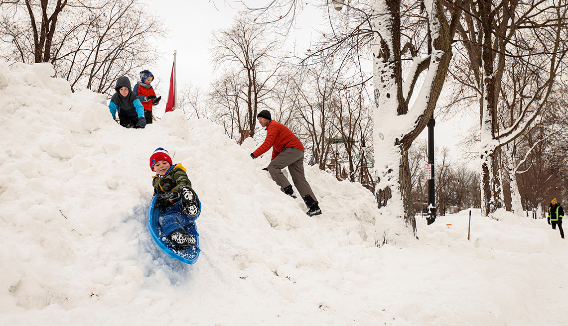 item 11 of Gallery image - a child sleds down a snow pile while two others wait and a man climbs up it