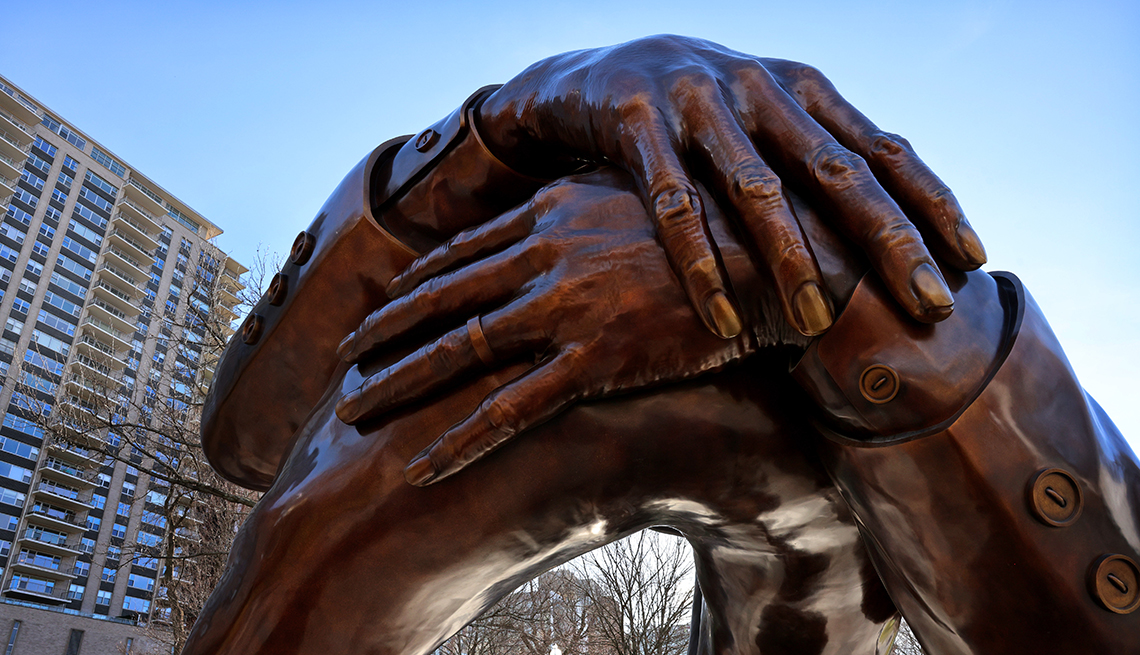 item 11 of Gallery image - a person looks up at the embrace, the m l k memorial sculpture in boston common, with tall buildings in the background
