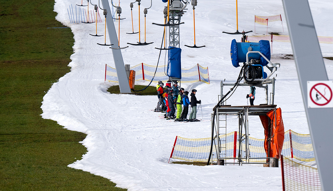 item 9 of Gallery image - skiers under a ski lift wait to hit the slopes, and behind them, very close by, the snow abruptly ends on green grass