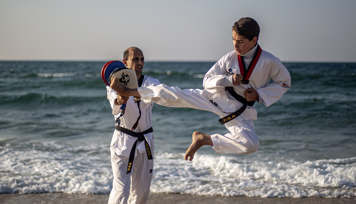 item 12 of Gallery image - two people doing tae kwon do on the shoreline, one standing, the other several feet in the air in a high kick  