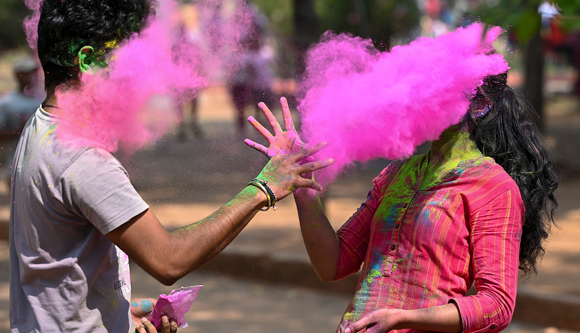 item 16 of Gallery image - two people whose faces are mostly obscured throw pink powder at each other during  celebration of holi holiday