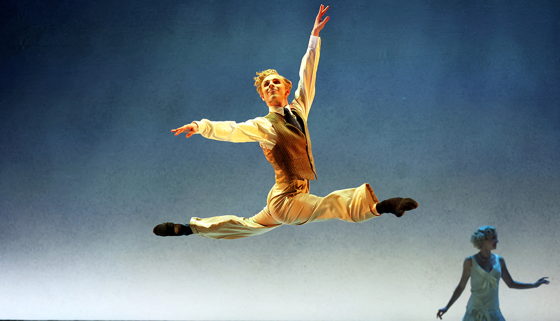 item 14 of Gallery image - a ballet dancer leaps in the air in a full split, and another dancer is in the background