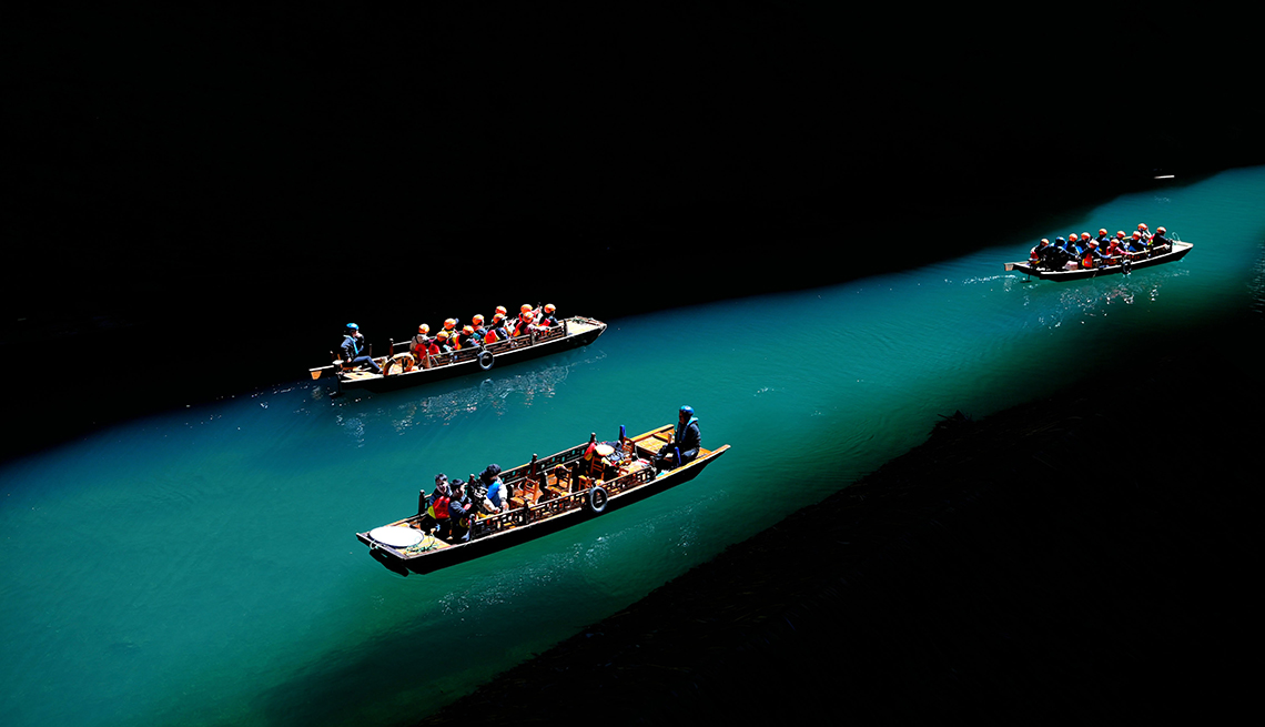 item 17 of Gallery image - three boats carrying people move through green water lit by a shaft of light through darkness
