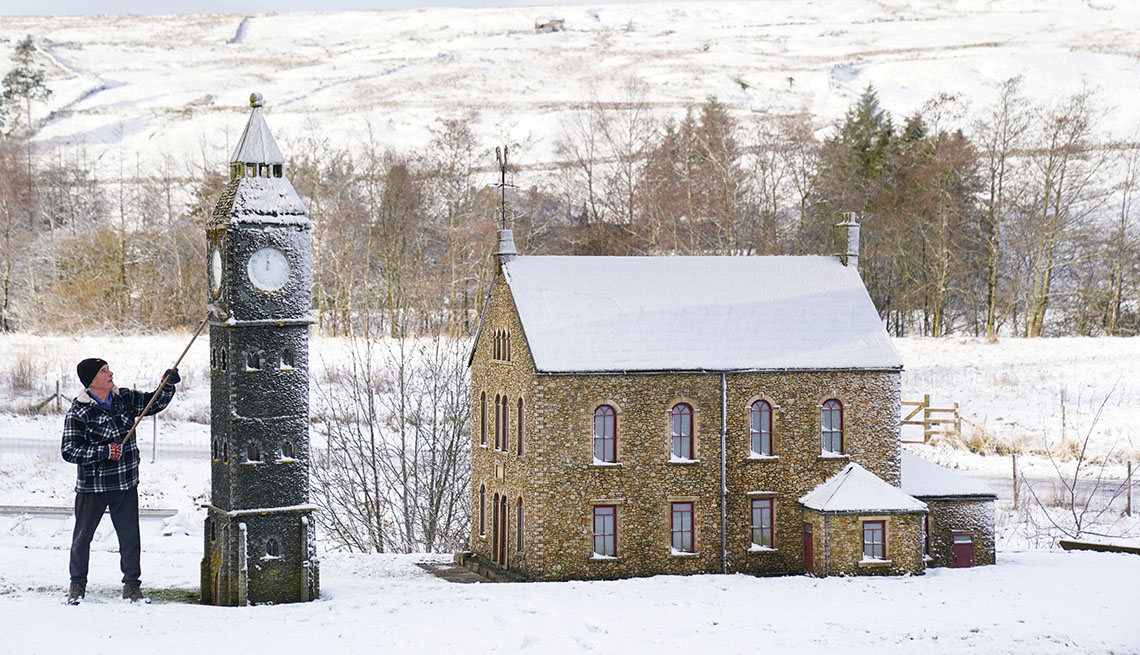 item 15 of Gallery image - a man clears snow from a clock tower next to a building in a model village