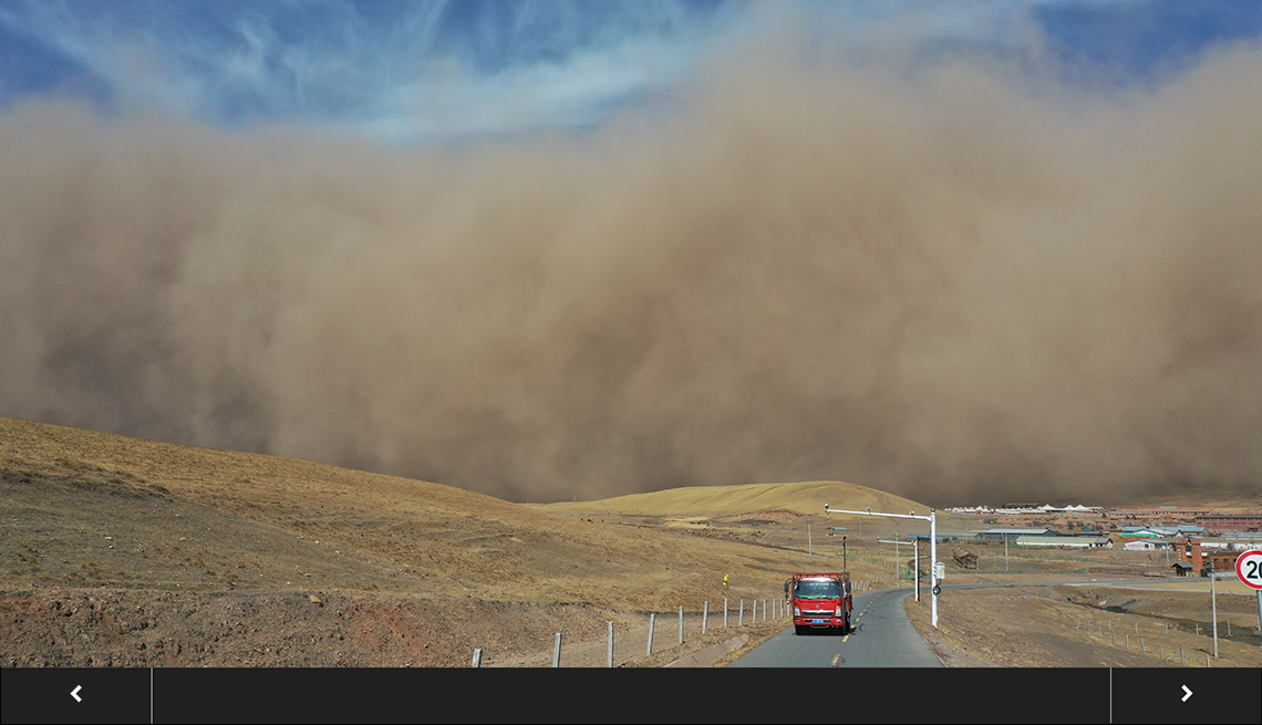a bus travels on a rural road with an enormous sandstorm looming in the background against a blue sky