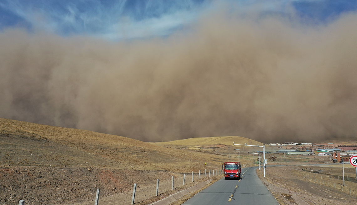 item 4 of Gallery image - a bus travels on a rural road with an enormous sandstorm looming in the background against a blue sky