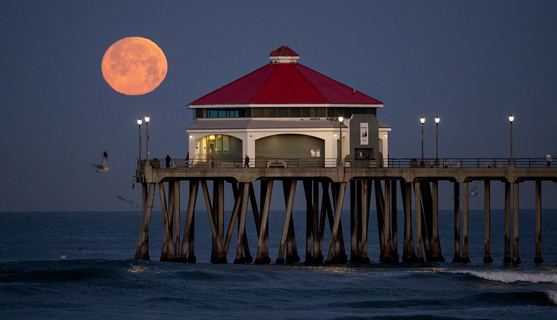 full pink moon at dawn over california's huntington beach pier