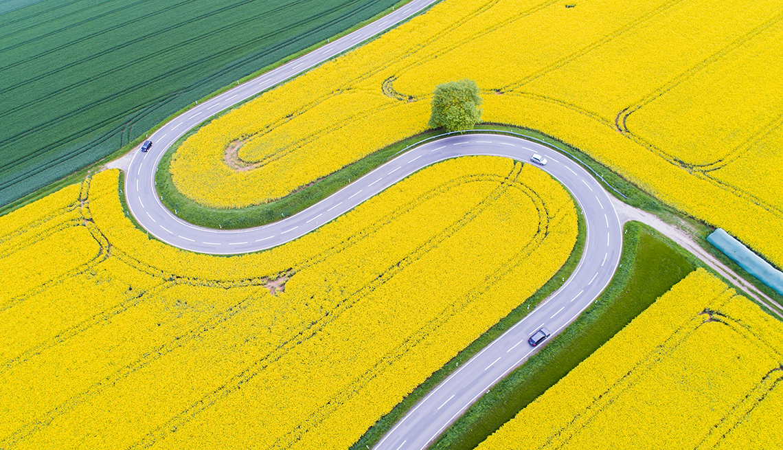 item 4 of Gallery image - aerial view of cars traveling on a winding country road in the shape of an S between rapeseed fields