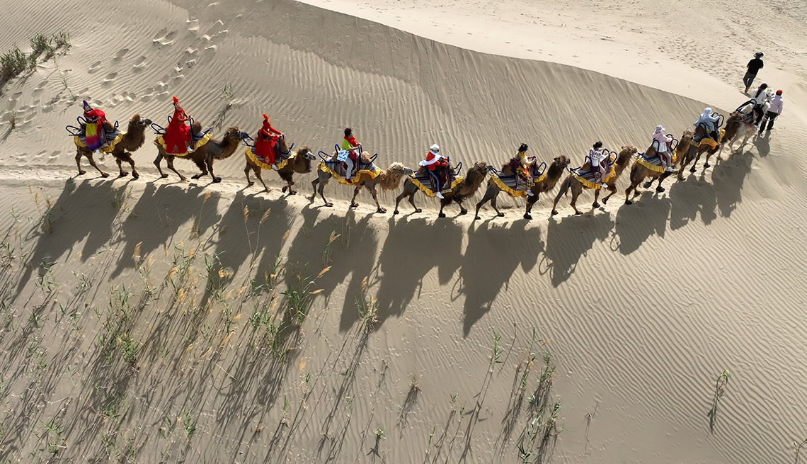 item 3 of Gallery image - aerial view of camels being ridden in a line across desert sand