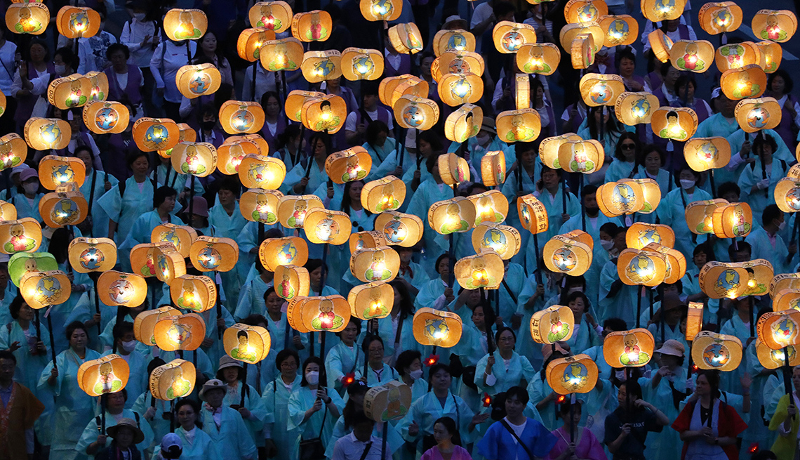 item 6 of Gallery image - a mass of people, many in white robes, carry glowing lanterns above their heads in a parade during the lotus lantern festival in seoul, south korea