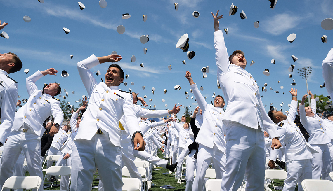 item 11 of Gallery image - naval academy graduates wearing white uniforms are standing in front of white chairs on a lawn throwing their hats in the air in celebration

