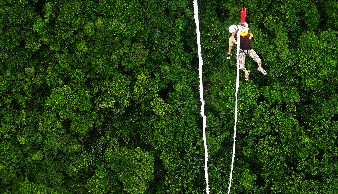 item 3 of Gallery image - a bungee jumper is suspended over dense green treetops