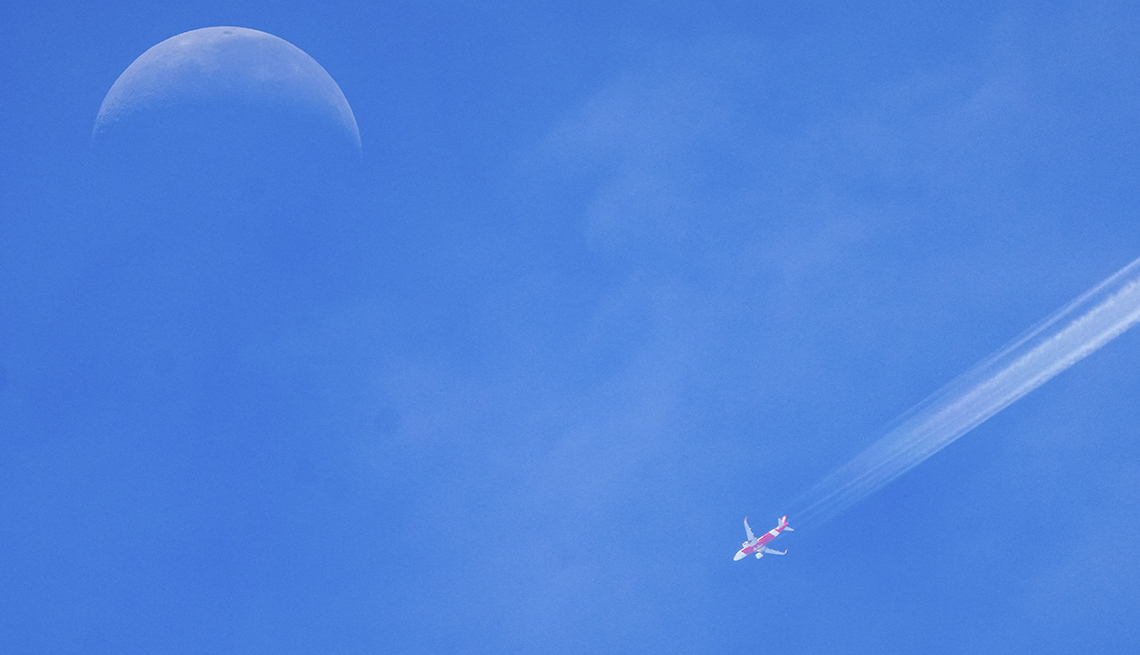 item 8 of Gallery image - An Air Asia airplane soars beneath a waning wedge of moon.