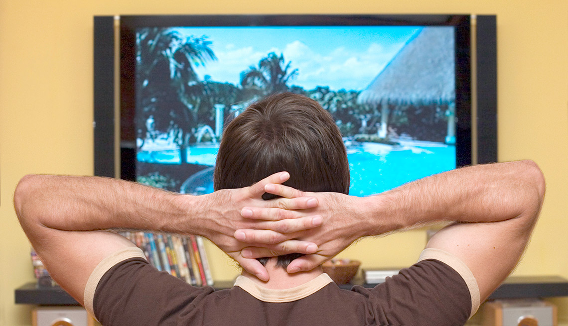 Hombre con las manos sobre la cabeza y viendo la televisión - Gana dinero desde casa.