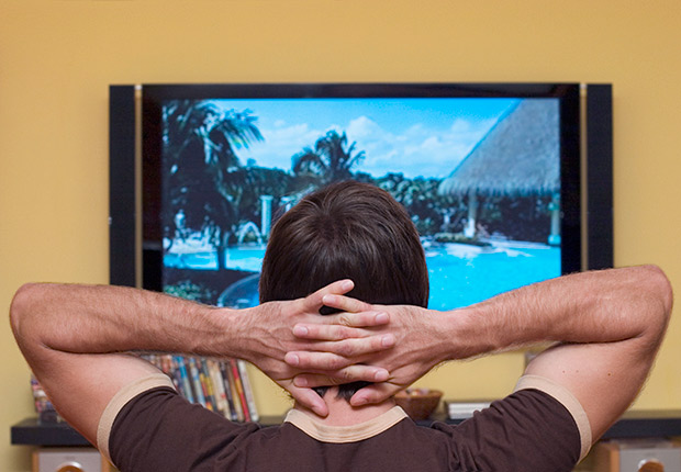 Hombre con las manos sobre la cabeza y viendo la televisión - Gana dinero desde casa.