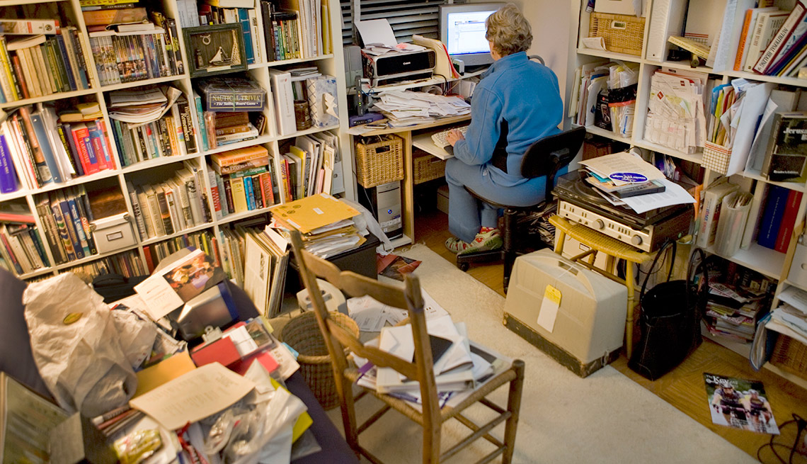 item 9 of Gallery image - Cuarto con estantes de libros, sillas, cajas y una mujer frente a un computador - Formas de reducir tu espacio