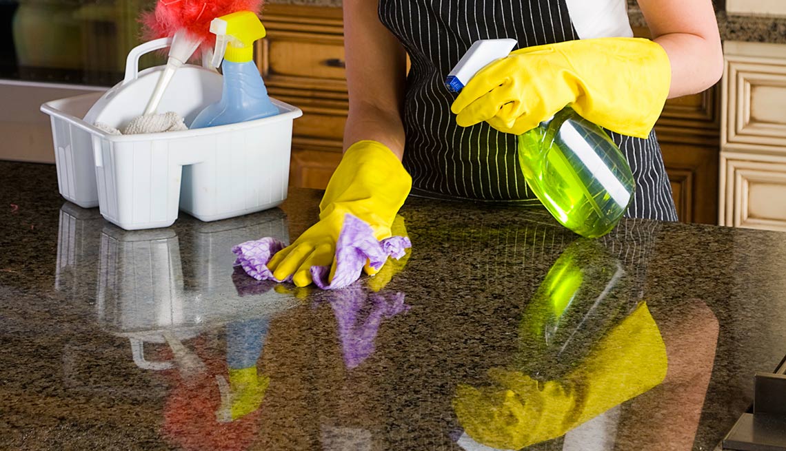 Mujer con guantes limpiando una superficie de granito - Evita reparaciones costosas en el hogar