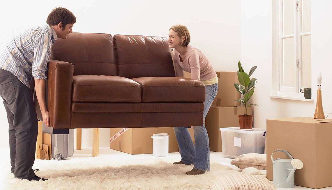 Hombre y mujer moviendo un sofá sobre un tapete - Evita reparaciones costosas en el hogar