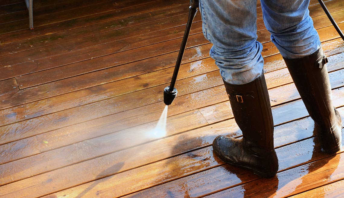 Hombre lavando piso de madera con una manguera a presión - Evita reparaciones costosas en el hogar