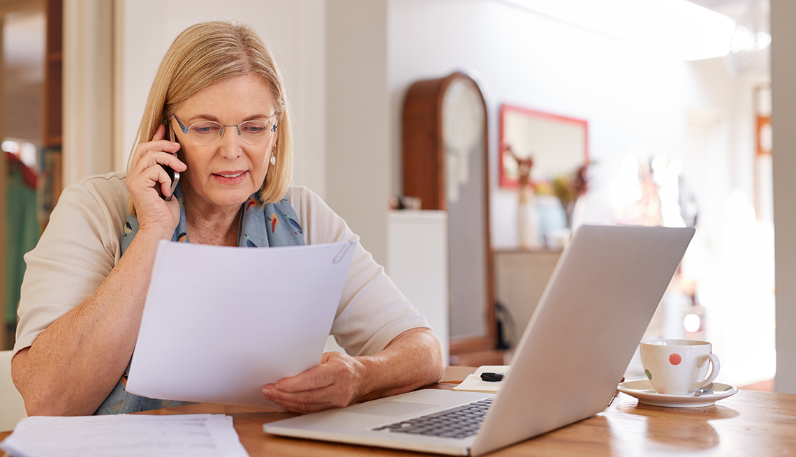 Mujer viendo papeles frente a una computadora personal mientras ve cómo reducir el costo de sus facturas