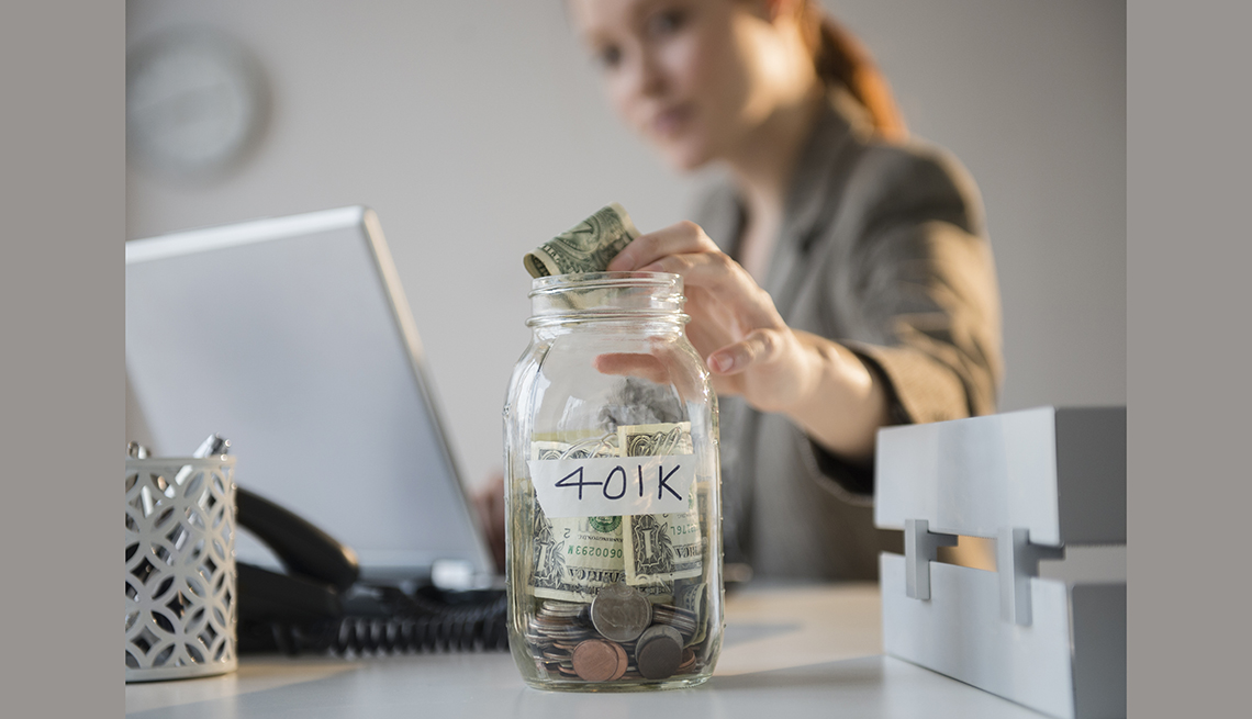 Mujer colocando dinero en un frasco de vidrio marcado con 401K - Cómo ahorrar 10 mil dólares al año
