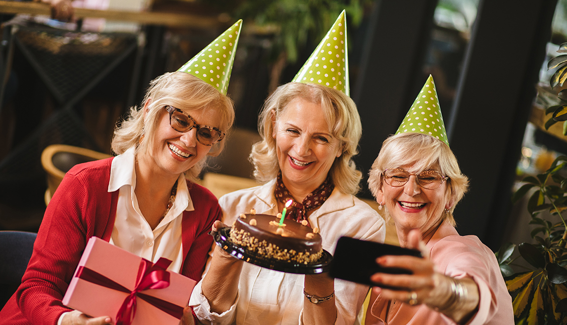 Senior ladies taking selfie while celebrating birthday in cafe with cake and gifts