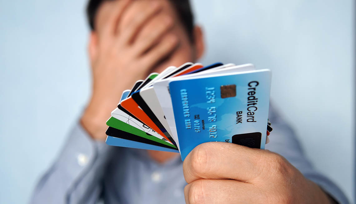 Hombre sostiene tarjetas de crédito en una mano y se cubre el rostro con la otra.