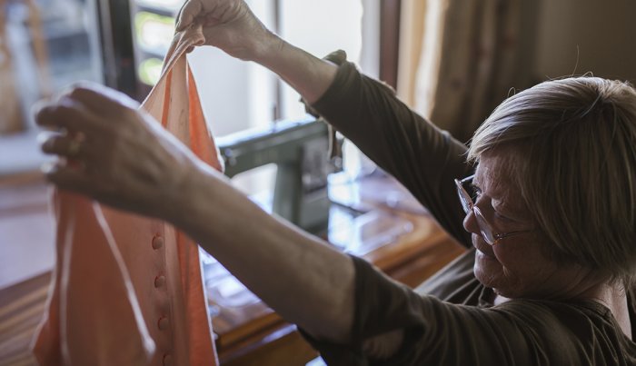 senior woman wearing glasses holds up a blouse to inspect it closely at home 