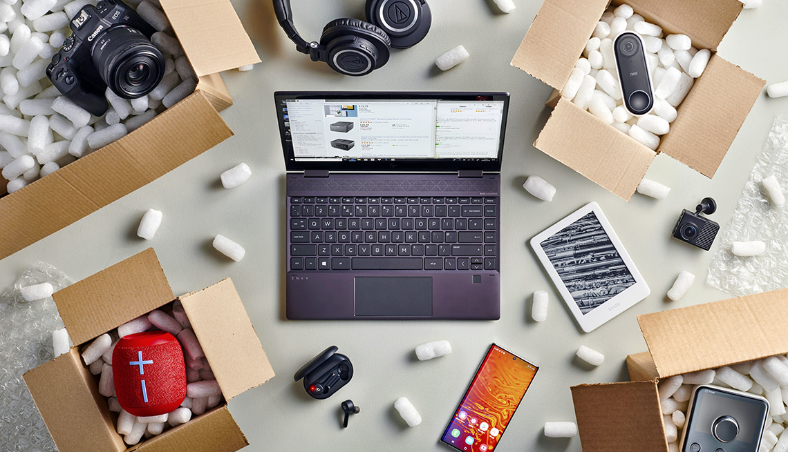 overhead photo of a laptop computer surrounded by online shopping purchases in open delivery boxes filled with packing peanuts
