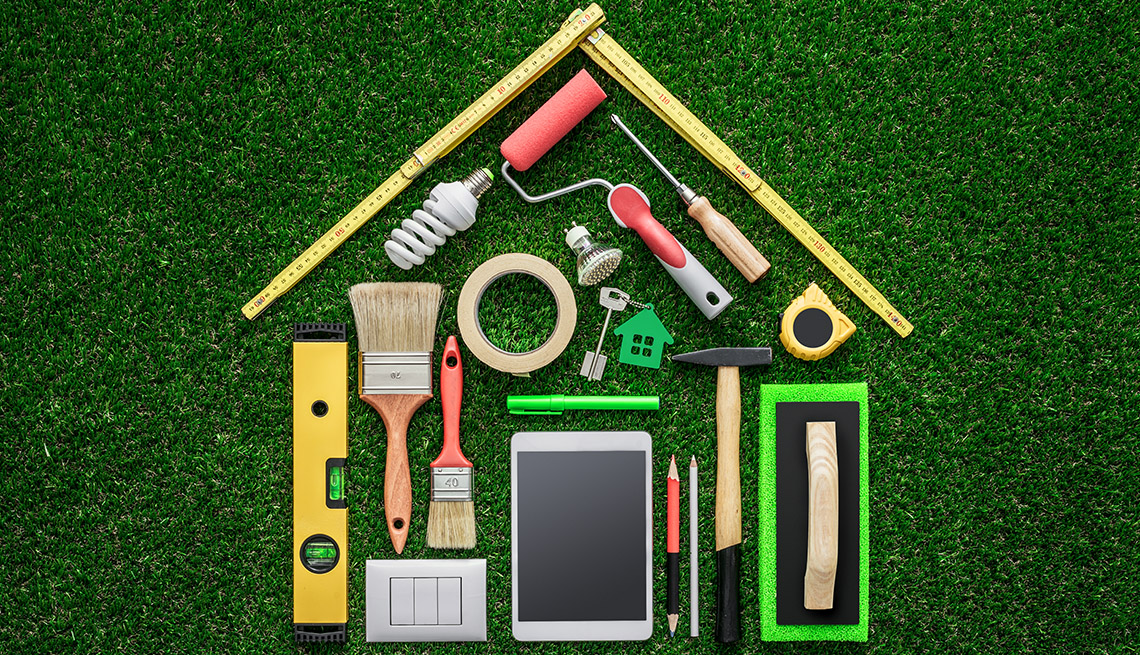 Home remodeling DIY tools spread out on a green grass background in the shape of a house 