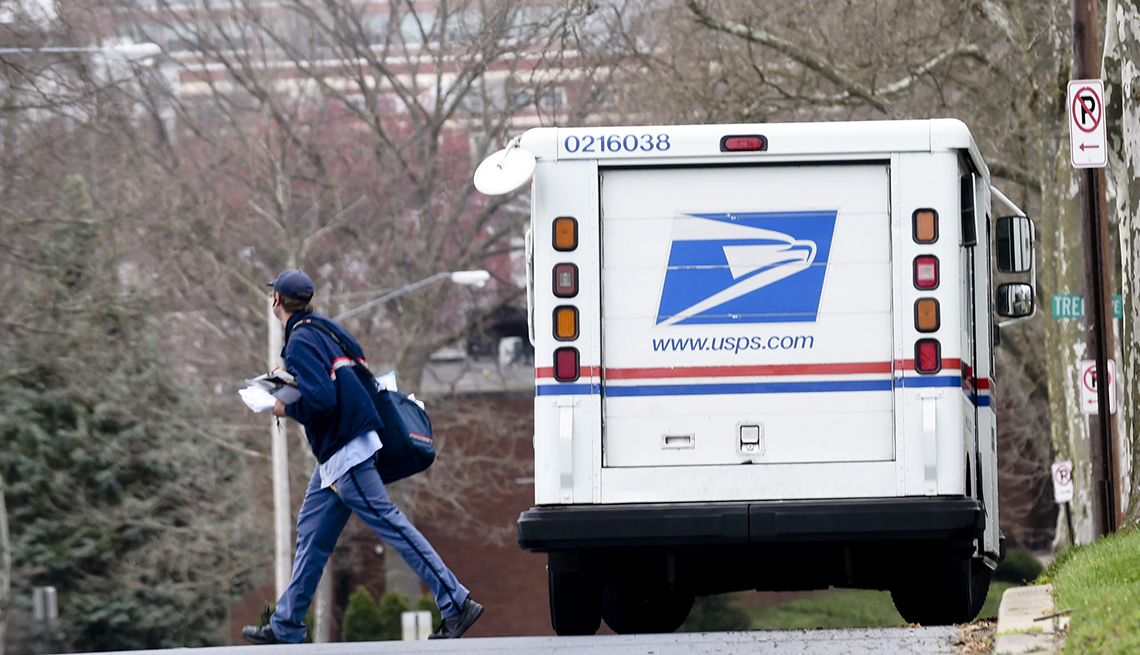 Camión del Correo Postal de Estados Unidos estacionado en una calle mientras el cartero cruza hacia el otro lado