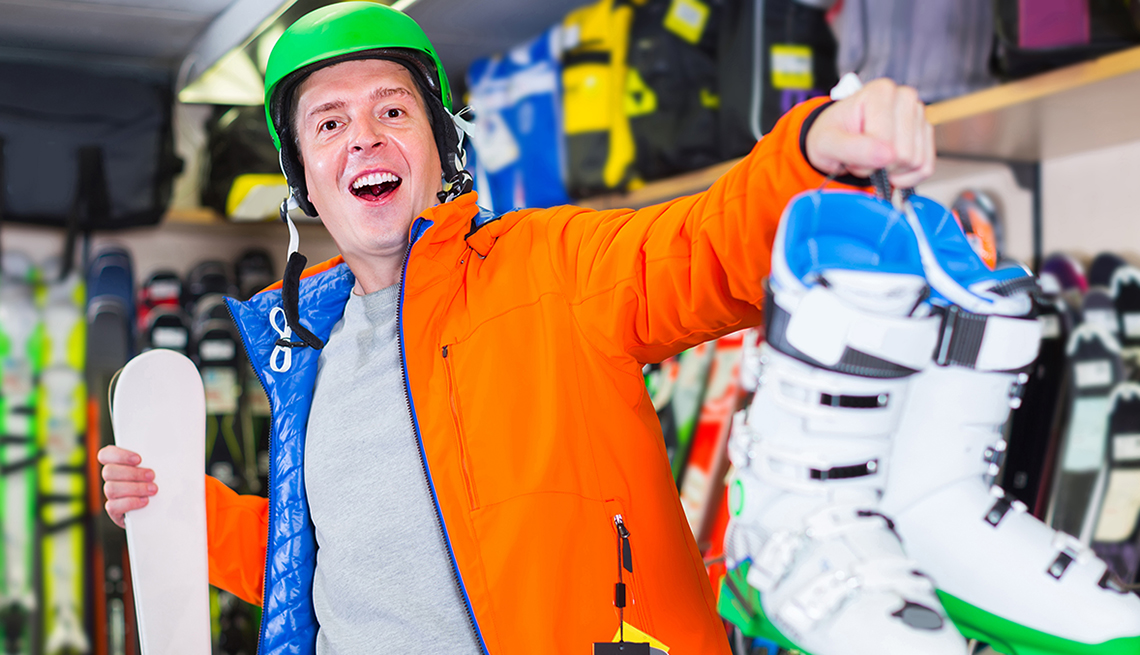 smiling man in ski shop trying on gear and holding up ski boots