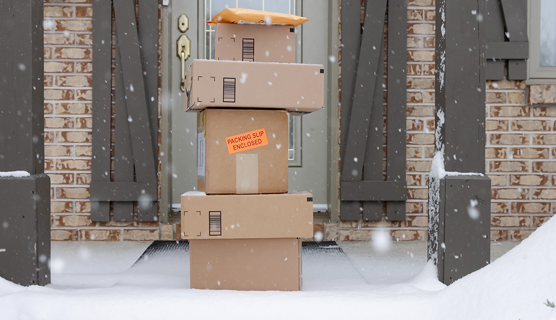 pile of delivered packages on the doorstep of a home while it is snowing 