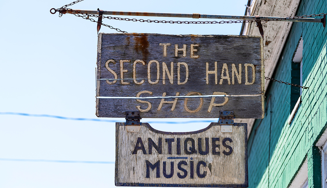 Hanging from a building exterior is a second hand shop sign with a sign underneath that says "Antiques - Music"
