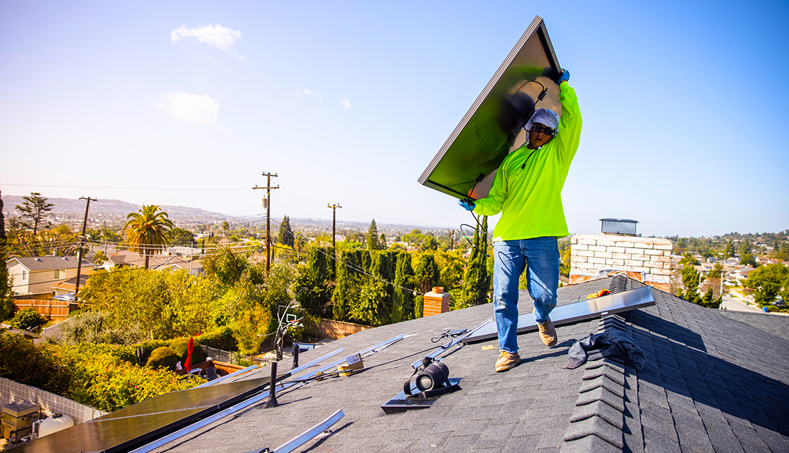 Trabajador carga un panel solar en su hombro mientras camina en el techo de una casa al sur de California