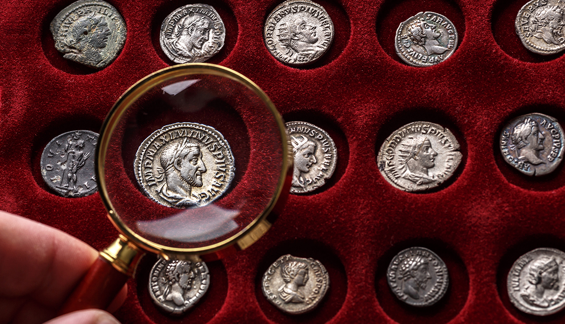 Mano sostiene una lupa sobre monedas de colección del Imperio Romano