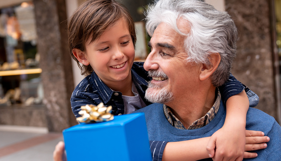 Un niño sonríe y abraza a su abuelo mientras le da un regalo de día del padre a su abuelo