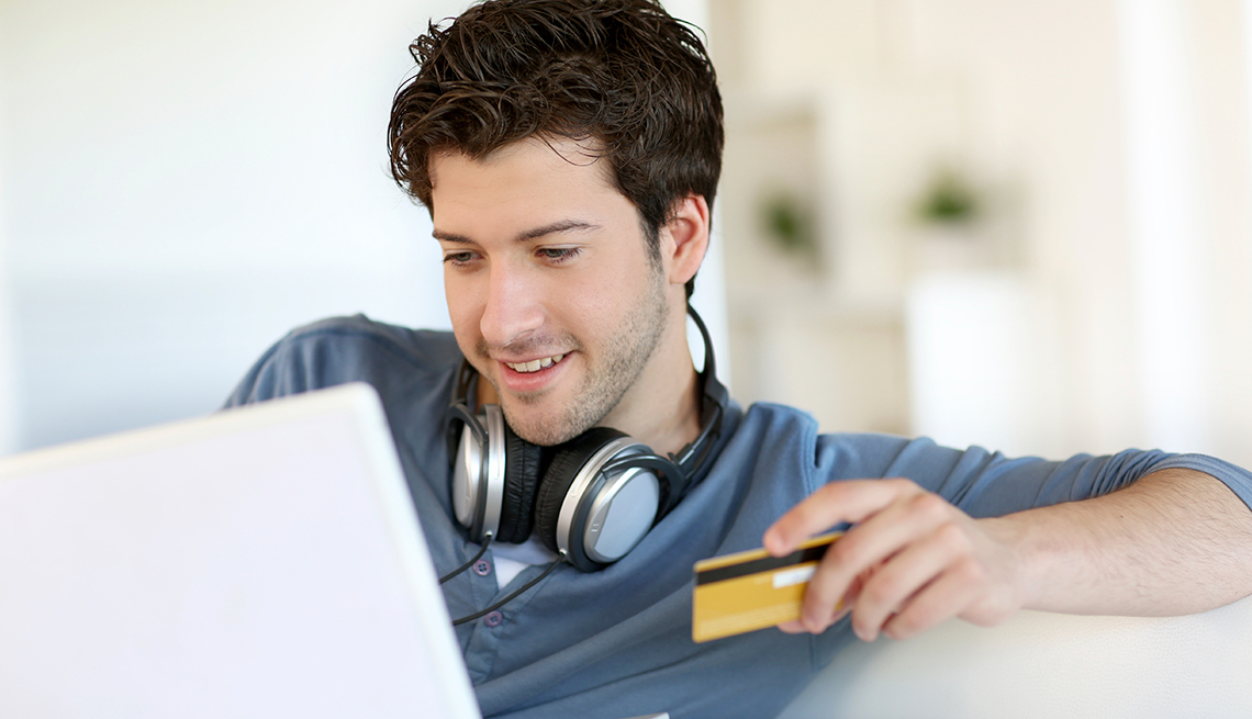 Hombre joven frente a una computadora portátil y con una tarjeta de crédito en la mano
